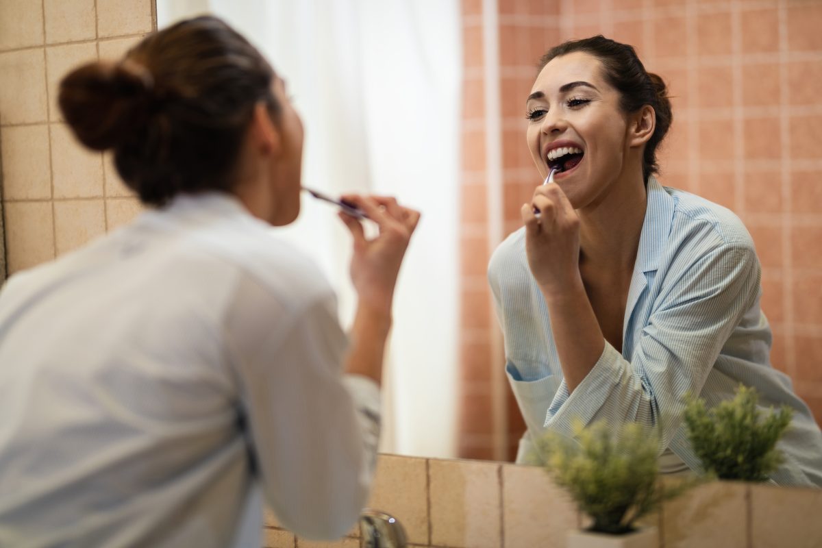 Reflection in a mirror of young woman brushing teeth in the bath
